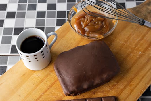 Close-up of chocolate-covered dessert with caramel and coffee on wooden board.